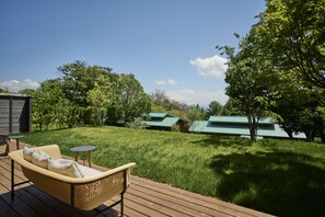 A wooden deck with a wicker sofa and two small tables, a grassy lawn, and several buildings with green roofs in the background. - The Hiramatsu Karuizawa Miyota (Miyota)