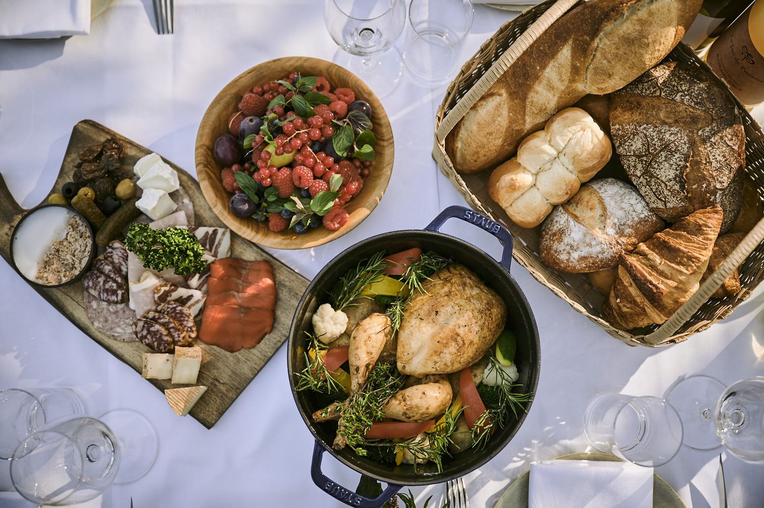 A table set with various food items including charcuterie, bread, and a pot of chicken with vegetables.