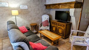 Ein Wohnzimmer mit einer Couch, einem Sessel, einem kleinen Tisch, einem Fernseher und einem Schrank.