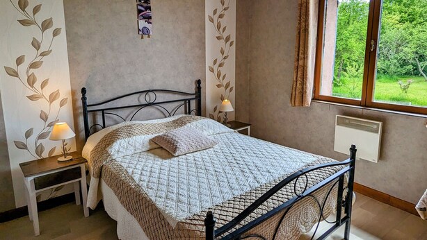 Ein Schlafzimmer mit Bett, Nachttischlampen, einem Wandbild und einem Fenster mit Blick auf Grünflächen.