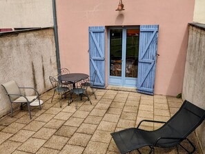 Een terras met een tafel, stoelen en een zwarte lounge fauteuil, en een blauwe deur.