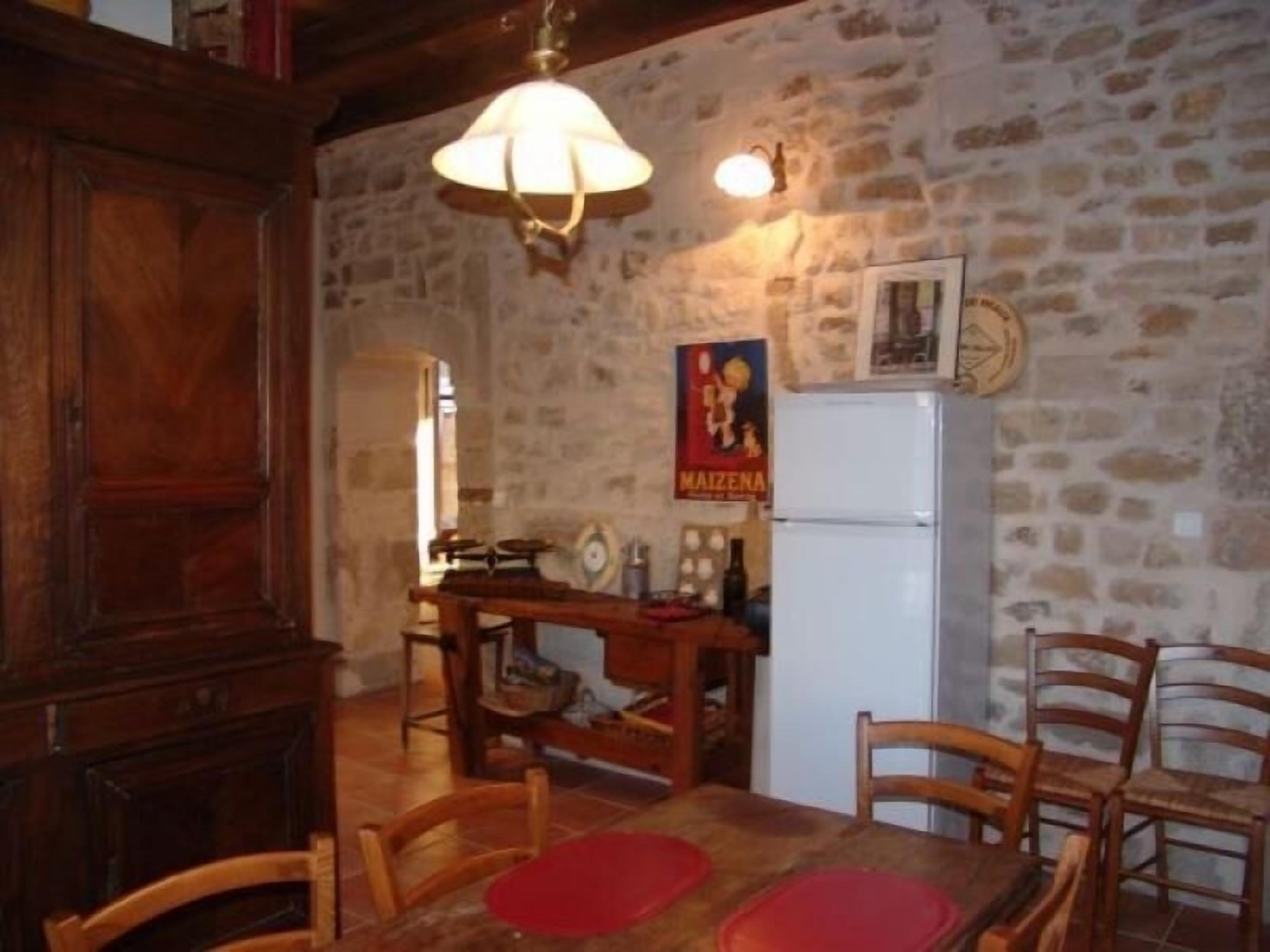A rustic kitchen with a stone wall, wooden furniture, a vintage refrigerator, and a poster on the wall.