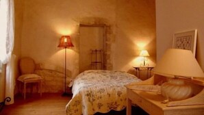 A cozy bedroom with a bed, two bedside lamps, a chair, and a small table. - Historic XIV Century Cottage with Modern Comforts, Garden and Parking (Void-Vacon)