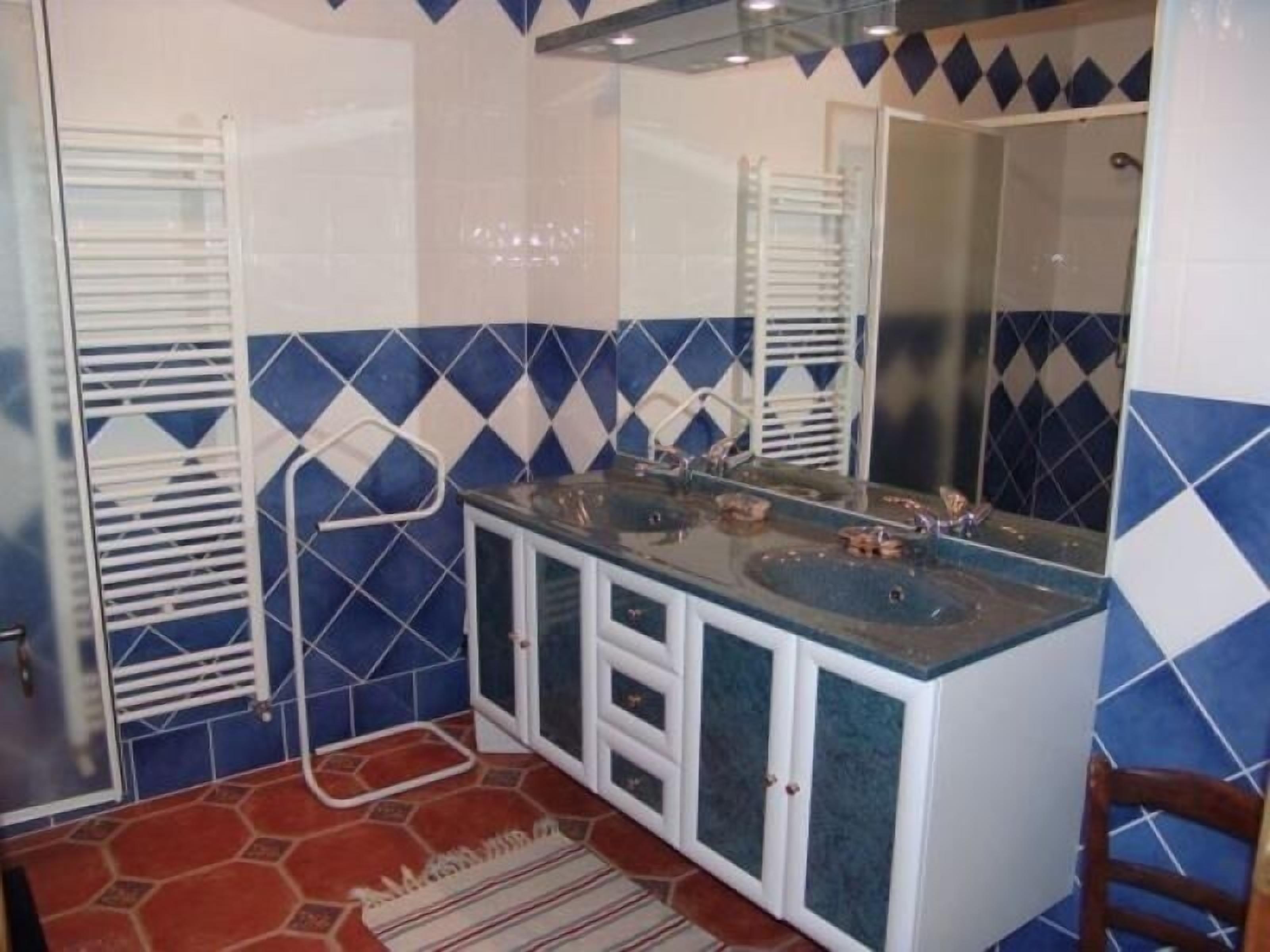 A bathroom with a glass-enclosed sink, white cabinets, and blue diamond-patterned tiles.