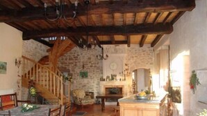 A rustic kitchen with exposed wooden beams, a stone wall, and a wooden staircase. - Historic XIV Century Cottage with Modern Comforts, Garden and Parking (Void-Vacon)