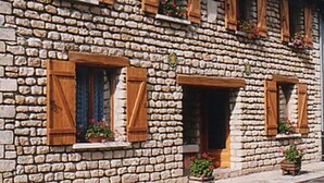 Un edificio de piedra con contraventanas de madera y macetas con flores.