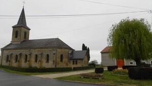 Una iglesia con un campanario alto y una pequeña torre de campanas, una calle pavimentada al frente y un sauce llorón grande a la derecha.