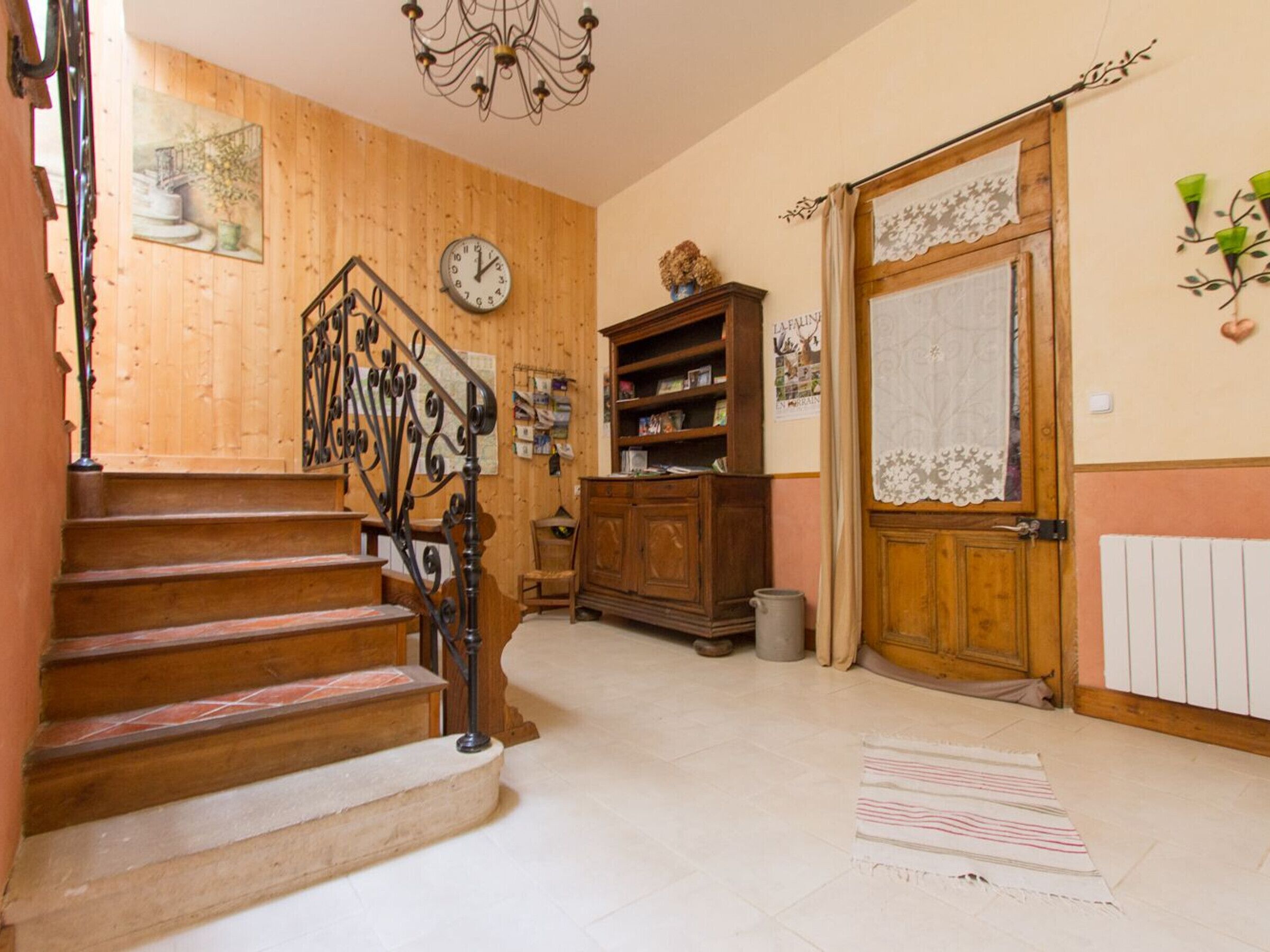 A wooden staircase with a black railing, a wooden door with lace trim, and a chandelier.