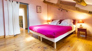 Un dormitorio con techo de madera, una cama con colcha rosa, dos lámparas de noche y suelo de madera.