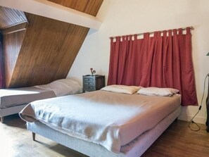 A bedroom with two beds, wooden ceiling beams, a red curtain, and a small dresser with a lamp. - Spacious Gîte for 12 with Fireplace & Garden, Opposite Thillombois Castle (Thillombois)