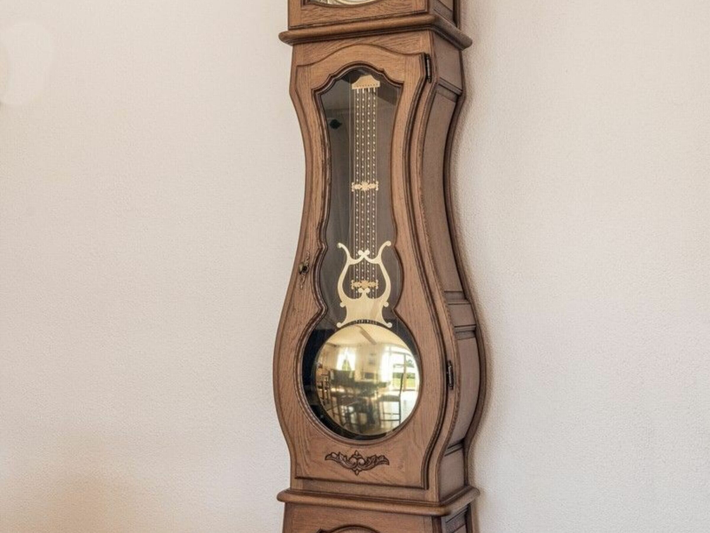 Un reloj de pie alto y ornamentado, con un espejo redondo grande en la parte inferior.