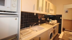 A compact kitchen with a microwave, sink, stove, and washing machine.