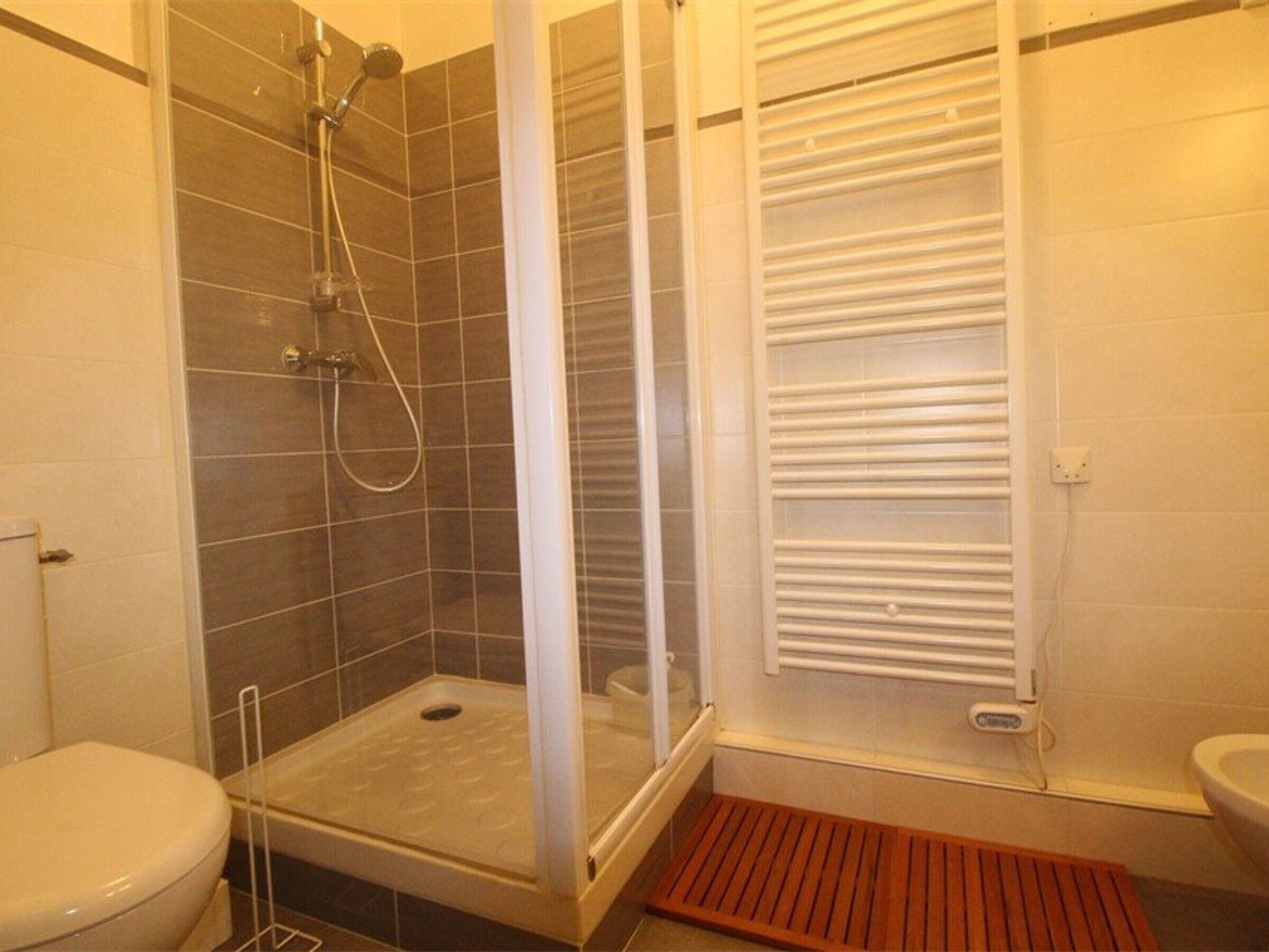Ducha con puerta de vidrio, inodoro blanco y barra para toallas.