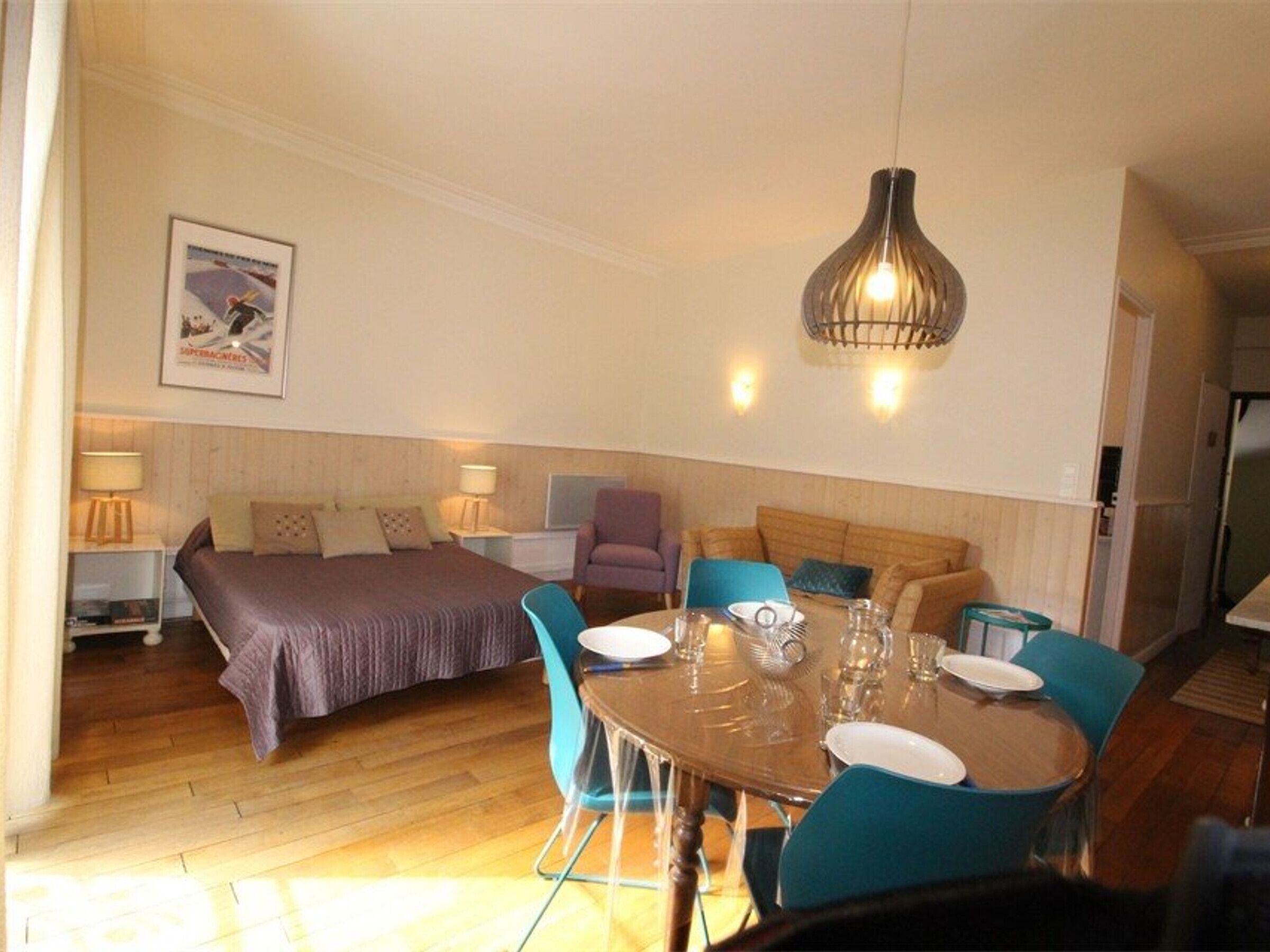 A hotel room with a bed, a dining table with chairs, a sofa, and a hanging light fixture.