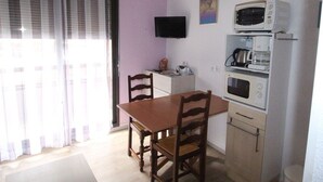 A small kitchen with a dining table and chairs, a microwave, a coffee maker, and a television on the wall.