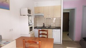 A compact kitchen with white appliances, a wooden dining table, and a small seating area.