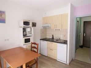 Une cuisine de taille réduite avec une table en bois, des appareils électroménagers blancs et des meubles de couleur claire.