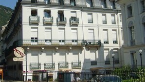 A multi-story building with balconies, a sign for a restaurant, and a fence in the foreground. - Central Apartment near Spa, 2 Bedrooms, Sleeps 6, Parking Included (Bagnères-de-Luchon)
