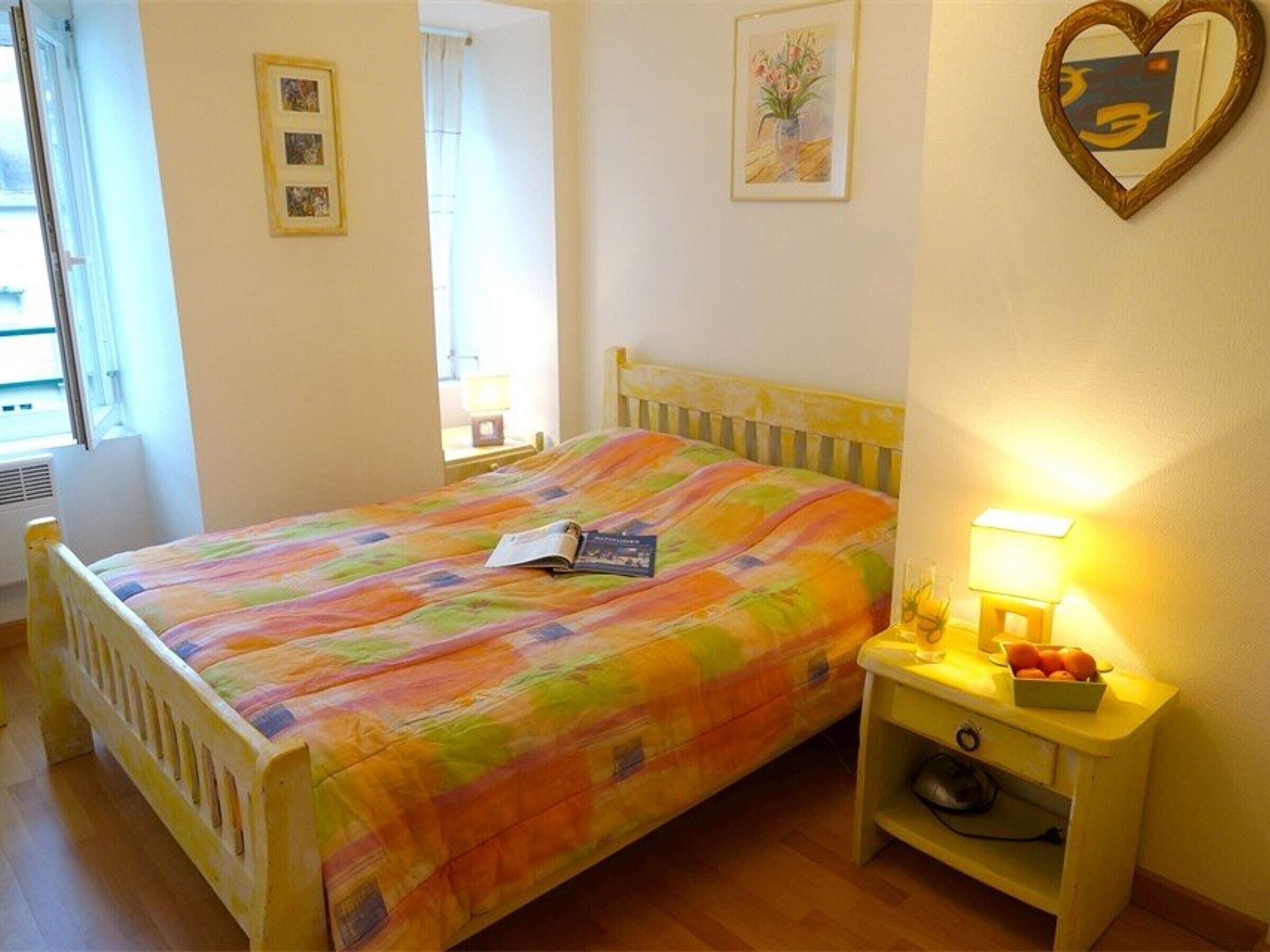 A bedroom with a bed, a bedside table with a lamp, and a wall with framed pictures.