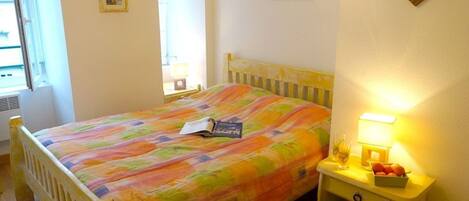 A bedroom with a bed, a bedside table with a lamp, and a wall with framed pictures.