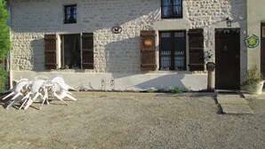 A stone building with two windows and a door, a sign with a logo, and outdoor chairs. - Charming Rural Retreat with Modern Amenities near Verdun – Pets Welcome! (Bréhéville)