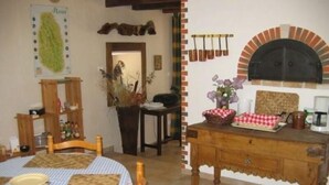 A cozy room with a wooden dining table, a small kitchen area with a pizza oven, and a rustic decor.