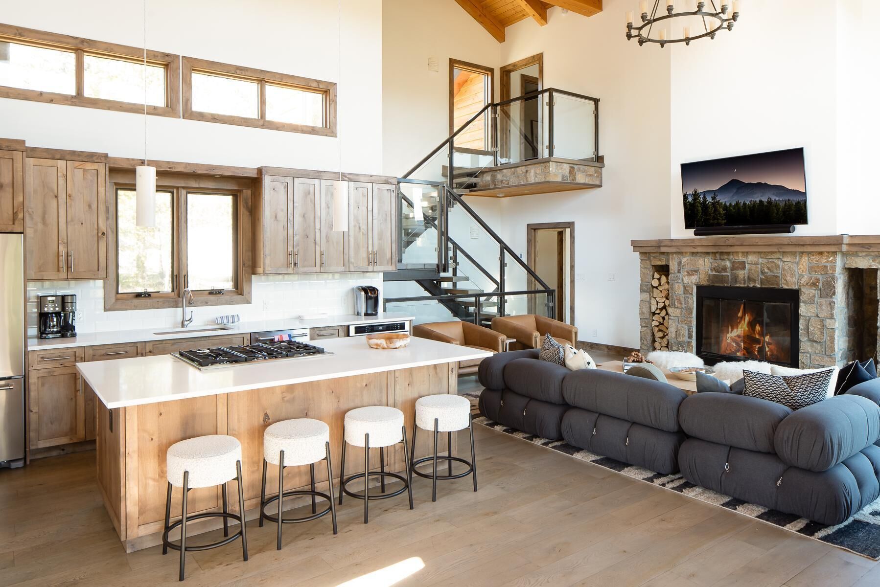 A spacious living area with a large sofa, a fireplace, a kitchen with wooden cabinets, and a staircase leading to an upper level.
