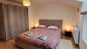 A bedroom with a large bed, two bedside lamps, a ceiling light, a radiator, and a skylight. - Charming Renovated Home near Verdun with Modern Amenities, Terrace, and Garden (Forges-sur-Meuse)