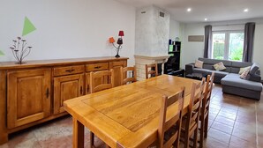 A living room with a wooden dining table, chairs, a sofa, and a fireplace. - Charming Renovated Home near Verdun with Modern Amenities, Terrace, and Garden (Forges-sur-Meuse)