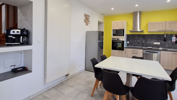 A modern kitchen with a white table and black chairs, a coffee machine, and a microwave. - Charming Renovated Home near Verdun with Modern Amenities, Terrace, and Garden (Forges-sur-Meuse)