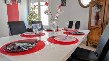 A dining table set with red placemats, clear glassware, and silverware, surrounded by black chairs.