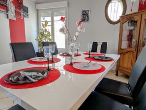 A dining table set with red placemats, clear glassware, and silverware, surrounded by black chairs.