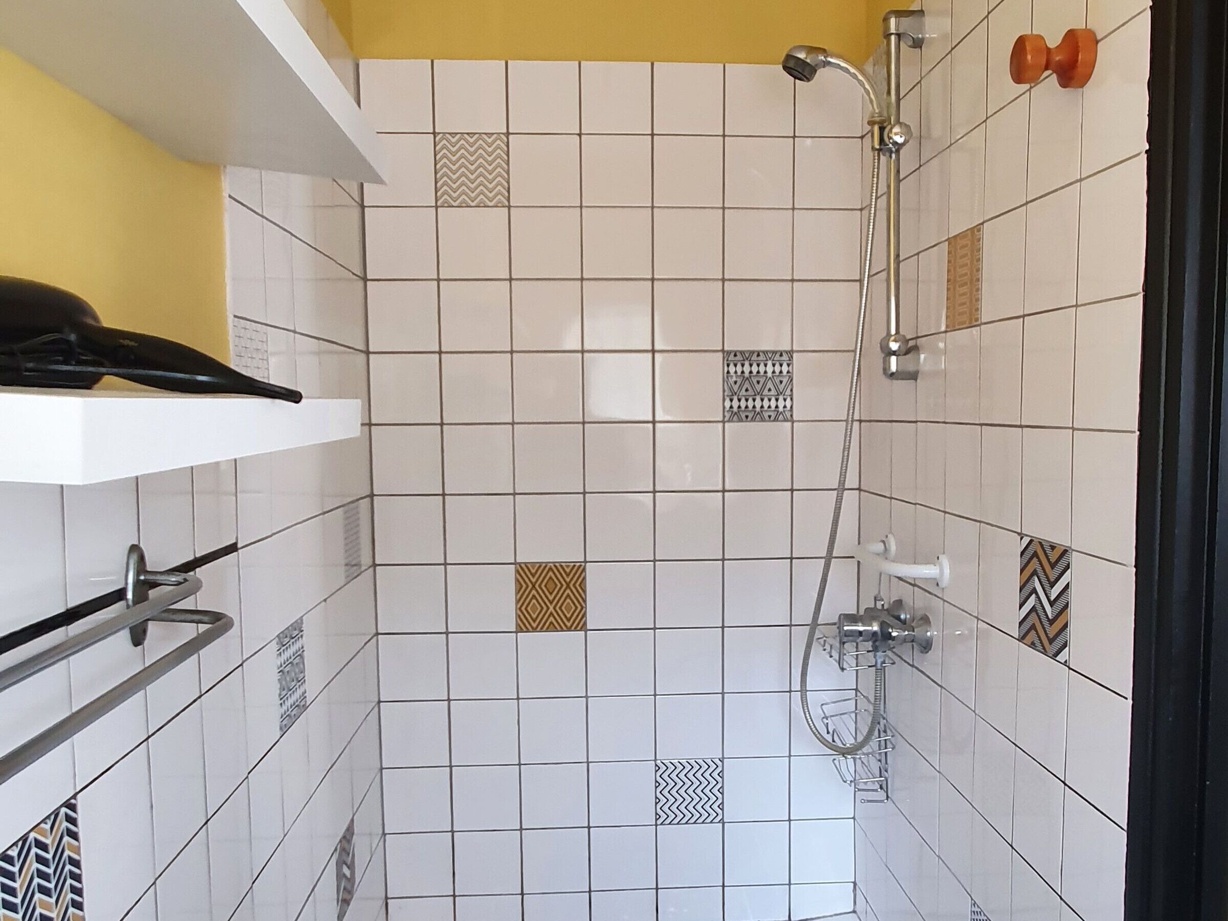 Une zone de douche carrelée, dotée d’un pommeau de douche à main et d’un robinet fixé au mur.