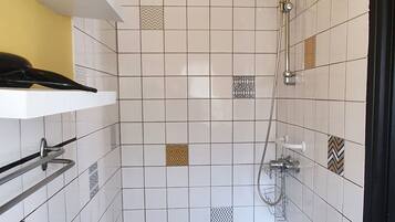 Une zone de douche carrelée, dotée d’un pommeau de douche à main et d’un robinet fixé au mur.