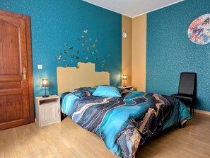 A bedroom with a bed, two bedside tables with lamps, a wooden door, and a wall with a circular design.