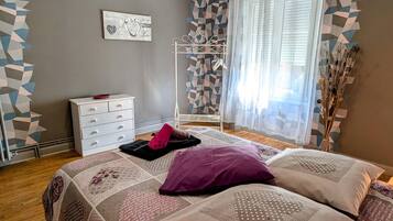 Une chambre à coucher avec un lit, une commode, un mur orné de motifs géométriques et une fenêtre avec des rideaux légers.