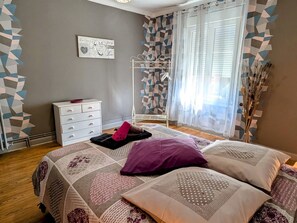 A bedroom with a bed, a dresser, a wall with geometric patterns, and a window with sheer curtains.