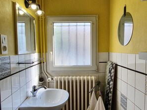 Un baño con lavamanos blanco, un espejo, una ventana y un radiador.