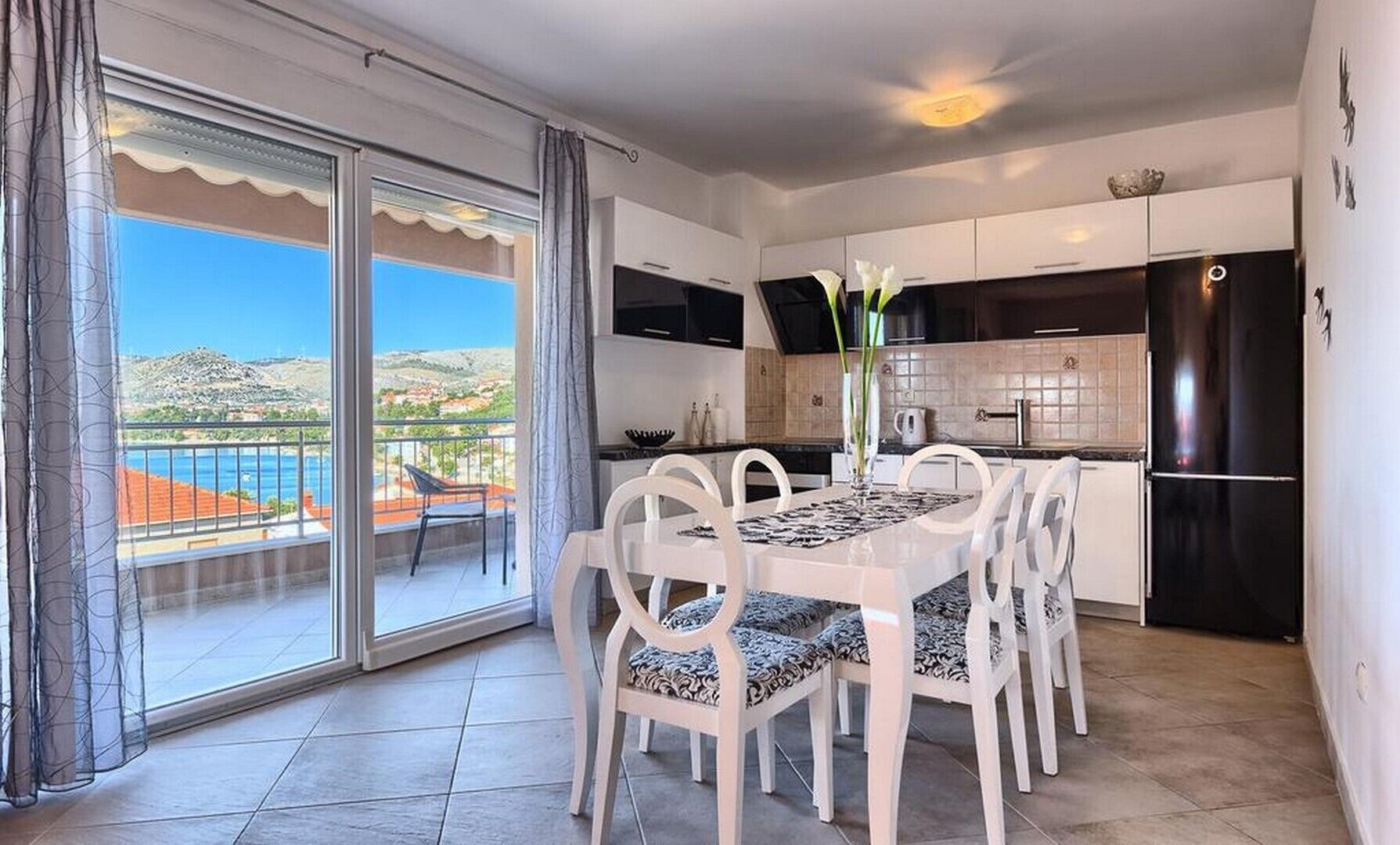 A dining area with a table and chairs, a kitchen with modern appliances, and a balcony with a view of the landscape.