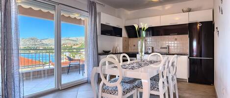 A dining area with a table and chairs, a kitchen with modern appliances, and a balcony with a view of the landscape.