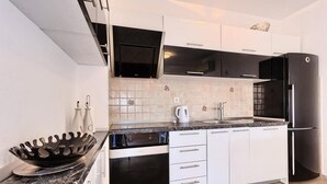 A modern kitchen with white cabinets, a black refrigerator, and a stainless steel sink.