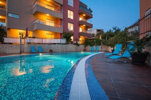 A swimming pool with a tiled edge, surrounded by lounge chairs and a stone wall.