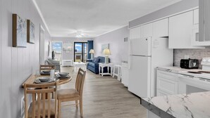 Una cocina moderna con armarios blancos, encimera de mármol y comedor con mobiliario de madera.
