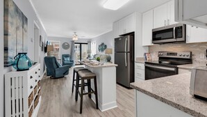 Una cocina moderna con armarios blancos, un refrigerador de acero inoxidable, un microondas y un horno. Cuenta con una barra con taburetes y un ventilador de techo.
