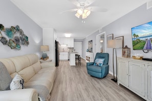 Una sala de estar moderna con un sofá, un sillón azul, un televisor y un elemento decorativo en la pared.