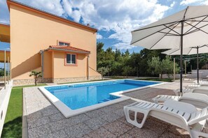 Une piscine entourée d’une maison et d’arbres, avec des chaises longues et un parasol.