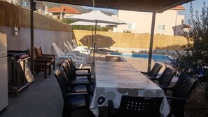 Un espace extérieur abrité, aménagé pour les repas, avec une piscine, des chaises longues et un barbecue.