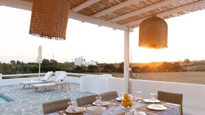 A terrace with a table set for dining, lounge chairs, and a view of the landscape. - Villa ILI - An Uncompromised luxurious escape  (Naxos)