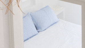 A white bed with a blue and white striped pillow and a white nightstand. - Villa ILI - An Uncompromised luxurious escape  (Naxos)