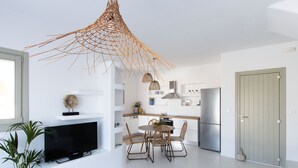 A modern kitchen with white cabinetry, a dining area with a round table and chairs, a TV on a stand, and a large window. - Villa ILI - An Uncompromised luxurious escape  (Naxos)